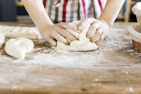 Baker's hands kneading dough at table in bakery