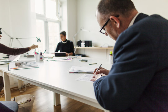 Rear view of businessman signing contract while businesswomen working in background