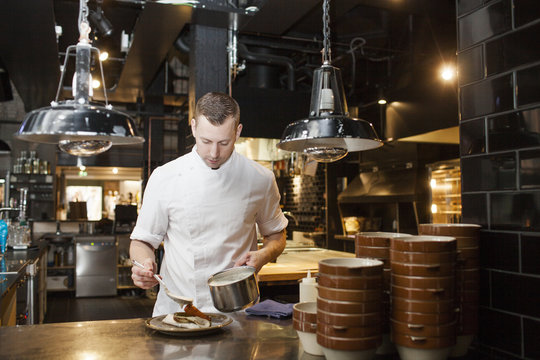 Young male chef preparing dish at counter in cafe