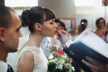 Brunette bride kisses a delicate wedding ring held by a priest