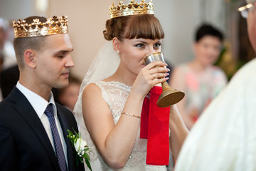 Smiling bride drinks holy wine standing in the front of a priest