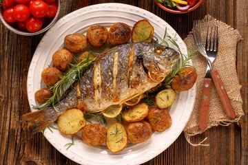 Foto op Plexiglas Vis Gegrilde vis met geroosterde aardappelen en groenten op het bord