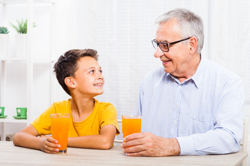 Grandfather and grandson are drinking orange juice at home. Healthy lifestyle.