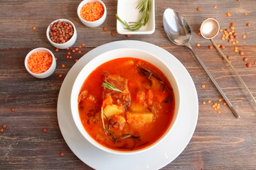 Lentil soup or mess of pottage in a white plate - composition with bowls, lentils, spoons on wooden table. Toned image.