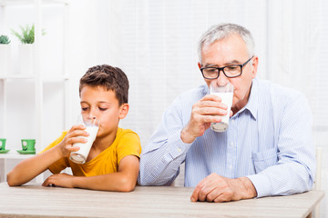 Grandfather and grandson are drinking milk at home. Healthy lifestyle.