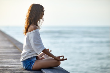 Fototapeta na wymiar Woman meditating in Lotus Pose on pier