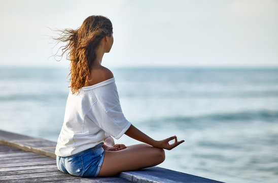 Woman meditating in Lotus Pose on pier