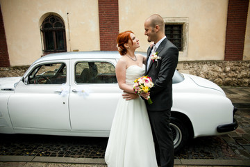 Stylish wedding couple stands before an old white car