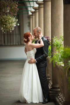 Red-haired bride kisses groom tender standing behind a pillar