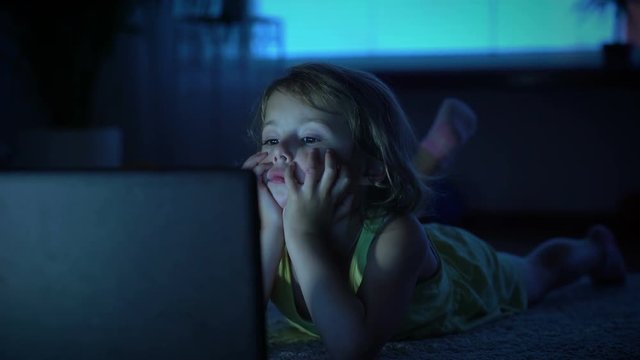 A little girl watches cartoons in the computer late in the evening.
