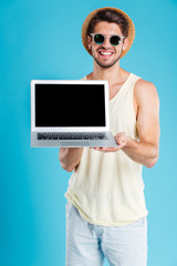 Cheerful young man standing and holding blank screen laptop