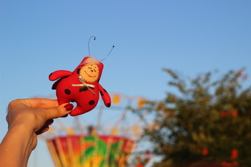 Fototapeta premium Textile handmade homemade toy fabric doll red spotted ladybug in a hand on a background of blue sky