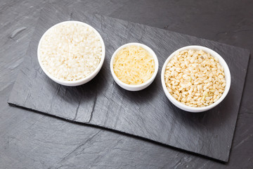 three kinds of uncooked rice in porcelain bowls on a tray slate
