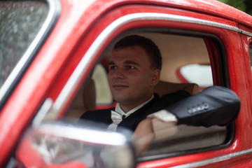 Man in black tuxedo looks confident driving a red car