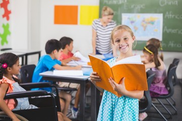 School girl holding a book in classroom