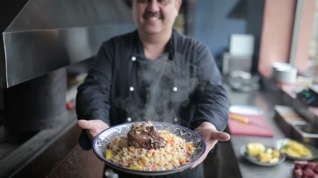 The chef shows on camera plate of pilaf with lamb.