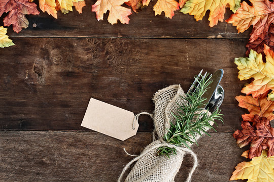 Silverware and burlap napkin with tag over rustic fall background of autumn leaves. Image shot from overhead.