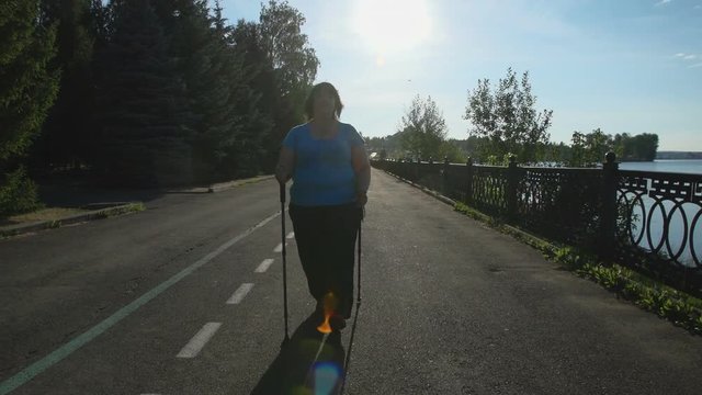 A woman walks through the Park with sticks for Nordic walking Sunny summer morning.