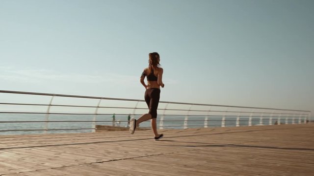 Young beautiful sportive girl jogging at seaside. Slow motion.