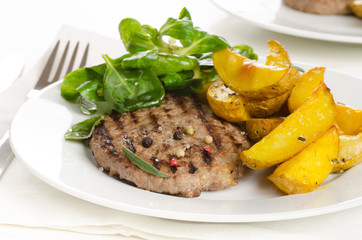 Beef burger patty with the roasted potato, side salad and spices on wh