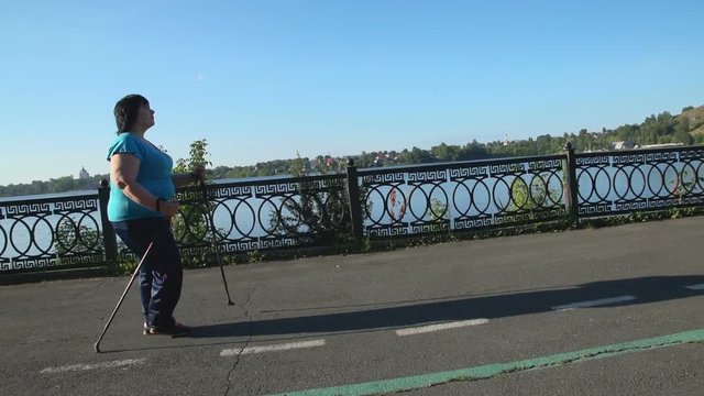 A woman walks through the Park with sticks for Nordic walking Sunny summer morning.