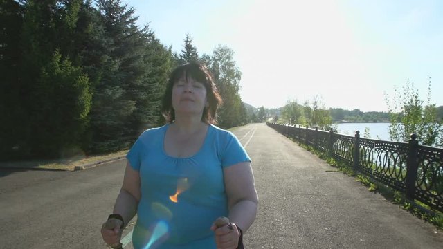 A woman walks through the Park with sticks for Nordic walking Sunny summer morning.