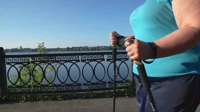 A woman walks through the Park with sticks for Nordic walking Sunny summer morning.