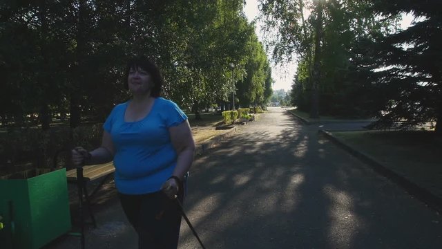 A woman walks through the Park with sticks for Nordic walking Sunny summer morning.