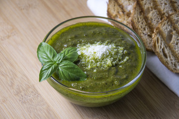 Green pesto with fresh basil leaves in small glass bowl on wooden background