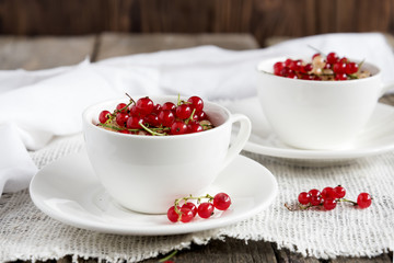 Two white cups with red currant. Wooden background.