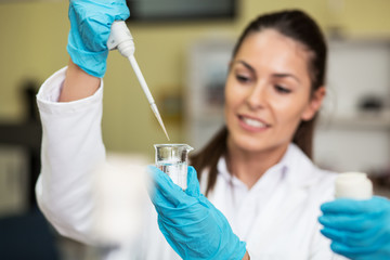 Young female scientist in lab coat wearing gloves, doing experiments in lab.