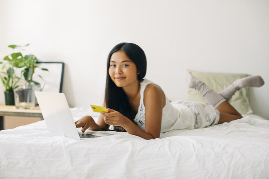Young woman lying in bed shopping online