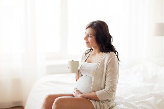 happy pregnant woman with cup drinking tea at home