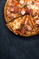 Pizza with cheese and sausage on a black background, top view