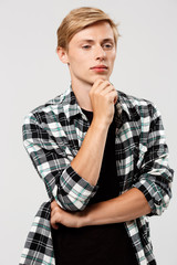 Confident thinking blond handsome young man wearing casual plaid shirt with hands crossed on chest looking away, copy space, grey background