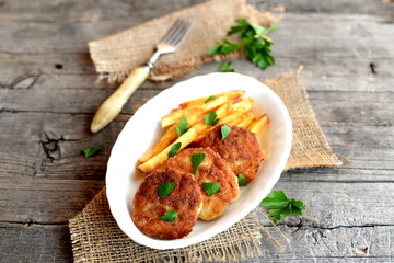 Meat patties and fried potatoes on a plate, a fork, a sprig of parsley and burlap on old wood background. Patties made with Turkey fillets and fried in olive oil