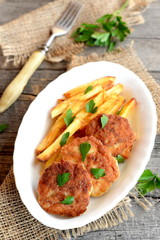 Meat patties served with fried potatoes. Turkey fillet burgers with potatoes on the plate. Fork, sprig of fresh parsley on an old wooden background. Lunch or dinner idea. Closeup. Top view