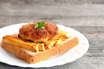 Sandwich with fried potatoes and meat cutlet on a plate and on old wooden table. A sandwich cooked from slice of white bread, fried potatoes and Turkey burger. Closeup
