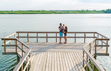 Happy young caucasian family with three year old daughter stand on a river pier.