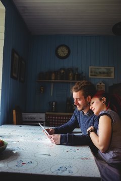Smiling young hipster couple using digital tablet in home