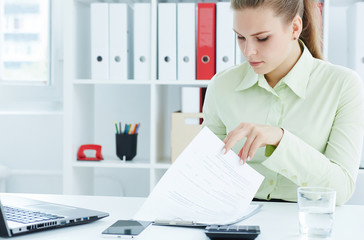 Beautiful young secretary making notes in the papers on the clipboard sitting at office. 