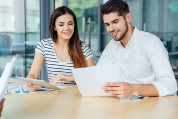 Smiling young couple with tablet sitting and working in office