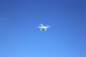 White drone  flying with camera record liens against blue sky