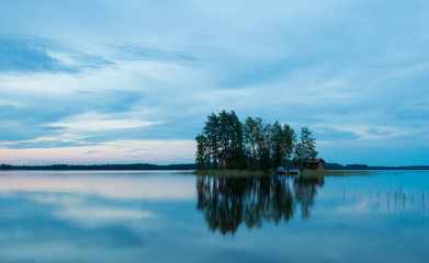 The island in the lake at sunset. The sky in the clouds. The smooth surface of the water.