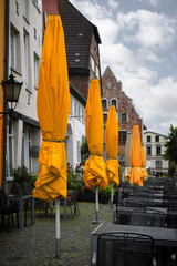 closed yellow sun umbrellas in a street cafe on a rainy summer day, old town of wismar, germany