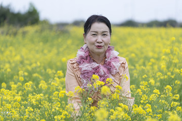 Naklejka na ściany i meble Portrait of happy mature asian woman in yellow flower garden ,rapeseed,canola flower.