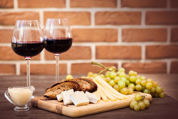 Cheese, toasted brown bread, two glasses of red wine. Horizontal.