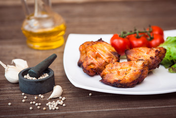 Juicy grilled pork fillet served with cherry tomatoes branch and lettuce on white plate. Background: wooden boards. Close-up. Horizontal.