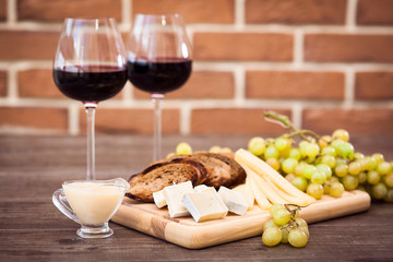 Cheese, toasted brown bread, two glasses of red wine. Horizontal.