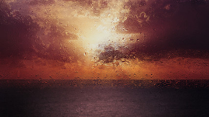 rain drops on a window in front of a beautiful ocean sunrise scene